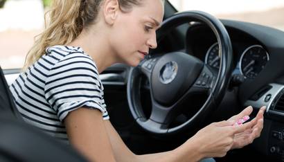 Jeune femme avec des médicaments dans la main au volant de sa voiture