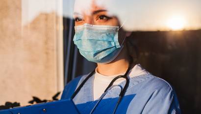 Young sad female caucasian UK US NHS EMS doctor carer looking through ICU window,fear uncertainty in eyes,wearing face mask gazing at sun,hope faith in overcoming Coronavirus COVID-19 pandemic crisis 