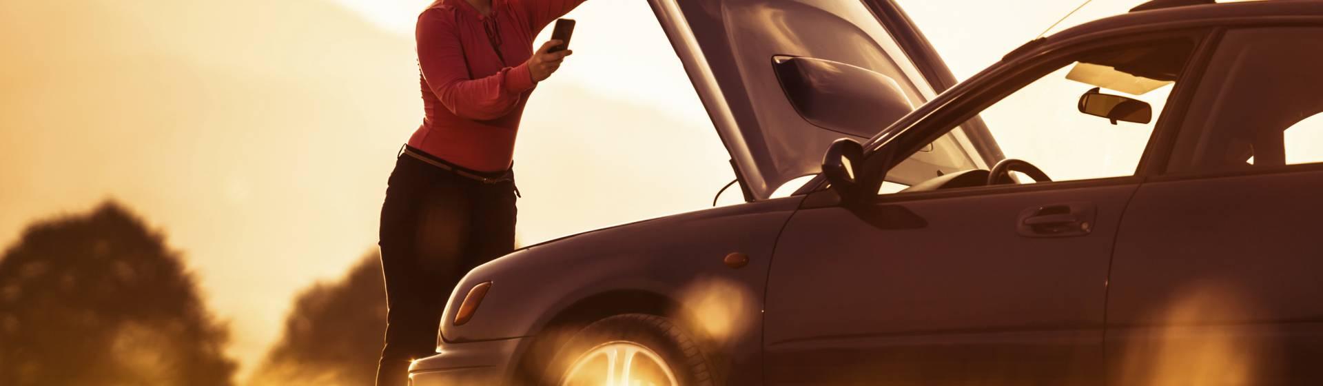 Femme au téléphone devant le capot ouvert de sa voiture en panne