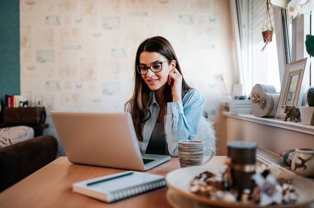 Young concentrated brunette woman in glasses working with laptop in her apartment.